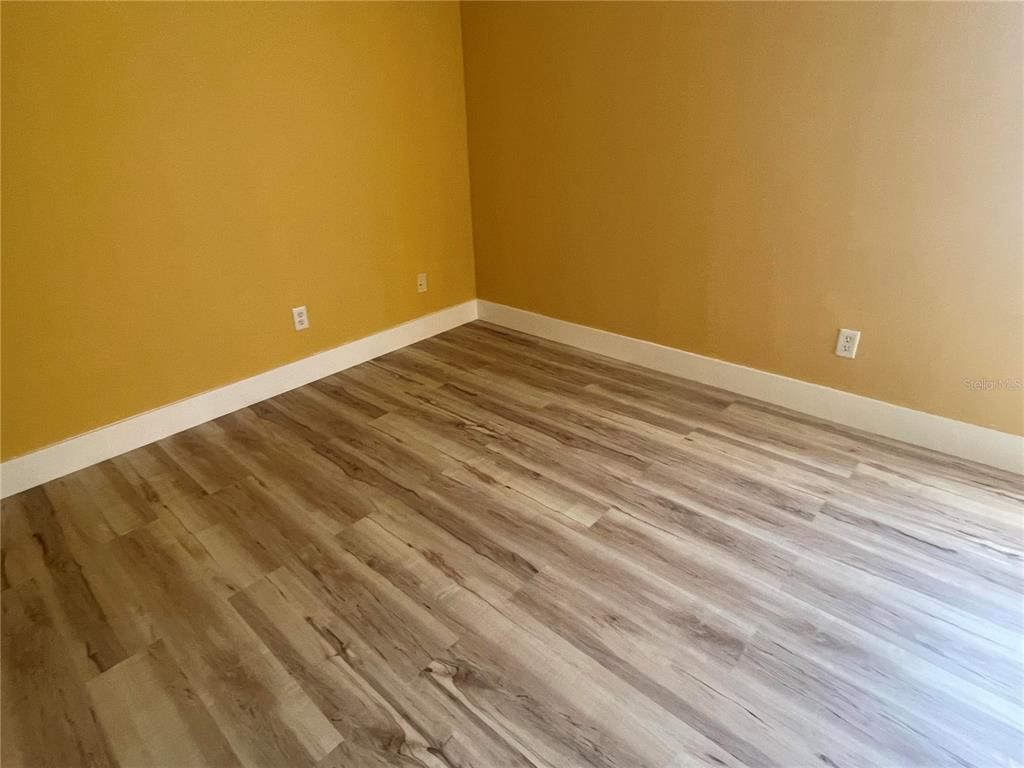 An empty room features mustard-yellow walls, white baseboards, and light-colored wood-look flooring — 759 FORDINGBRIDGE WAY, OSPREY, FL