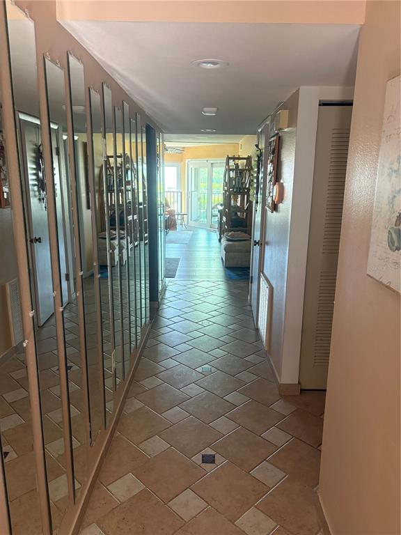 A hallway with tiled floors and a wall of mirrored closet doors leading to a balcony — 3705 E BAY DRIVE UNIT 103, BRADENTON BEACH, FL