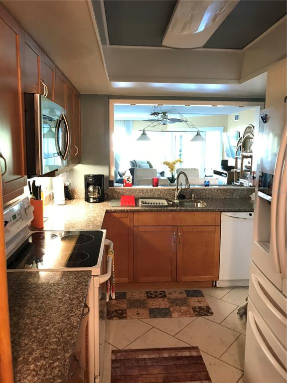 A kitchen features wood cabinets, granite countertops, stainless steel appliances, and a pass-through window — 3705 E BAY DRIVE UNIT 103, BRADENTON BEACH, FL