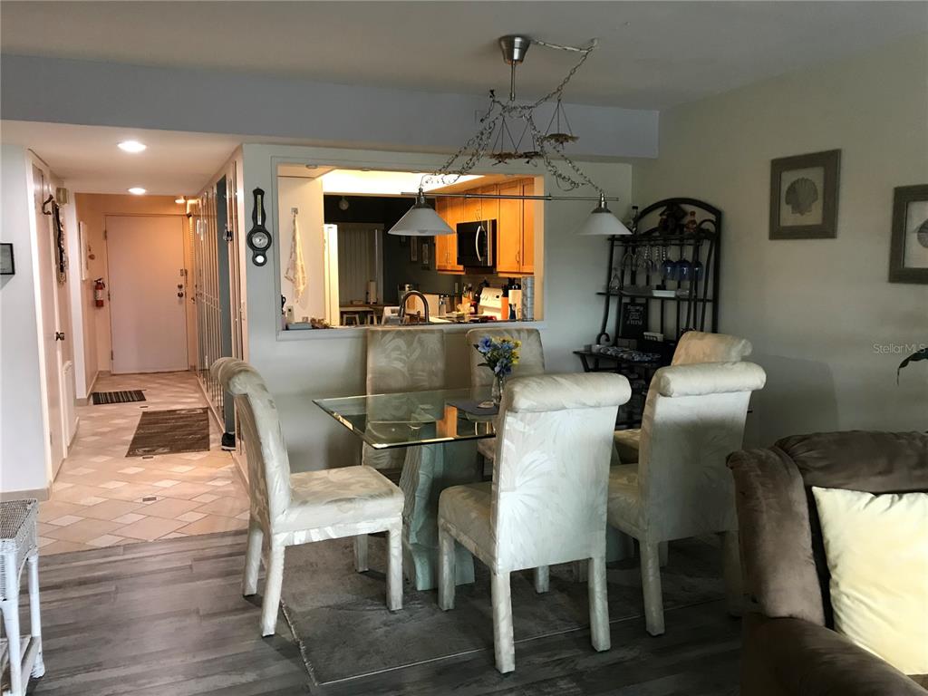 A dining area with a glass table and four chairs sits before an open kitchen — 3705 E BAY DRIVE UNIT 103, BRADENTON BEACH, FL