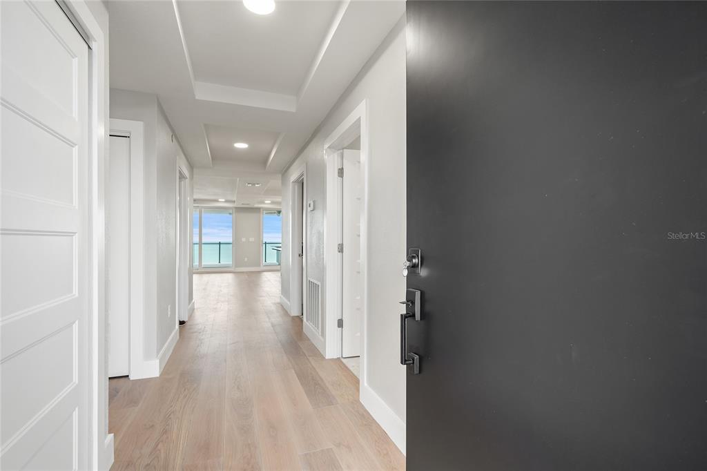 A hallway with light wood flooring leads toward a bright room with large windows — 14048 GULF BOULEVARD UNIT 402, MADEIRA BEACH, FL