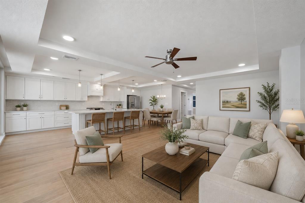 This open-concept living room and kitchen features white cabinetry, light wood flooring, and neutral furniture — 14048 GULF BOULEVARD UNIT 402, MADEIRA BEACH, FL