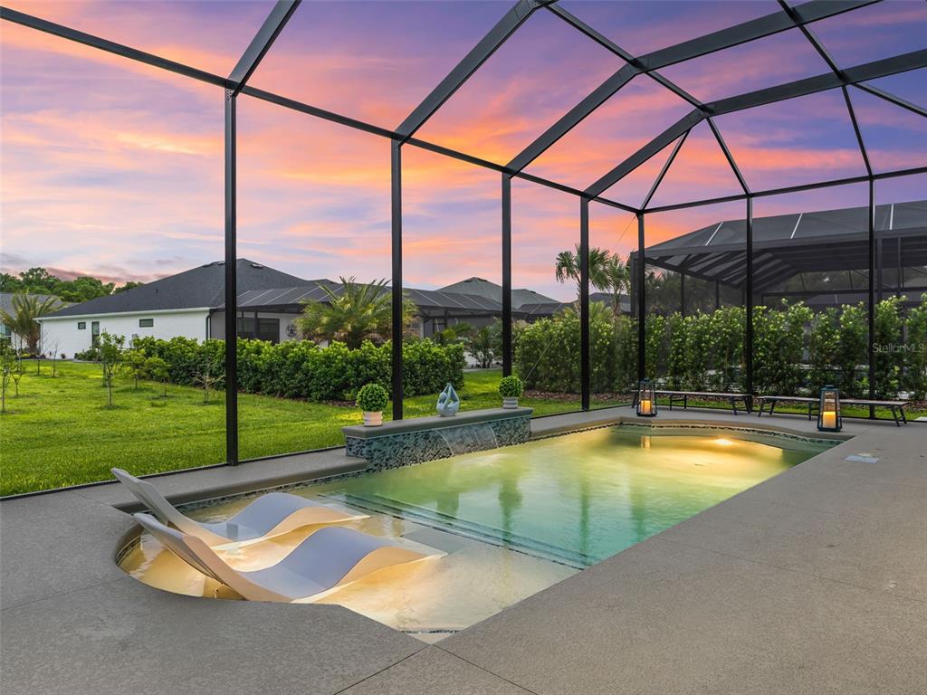 A swimming pool with lounge chairs and a water feature sits inside a screened enclosure — 7095 JENNINGS COURT, THE VILLAGES, FL
