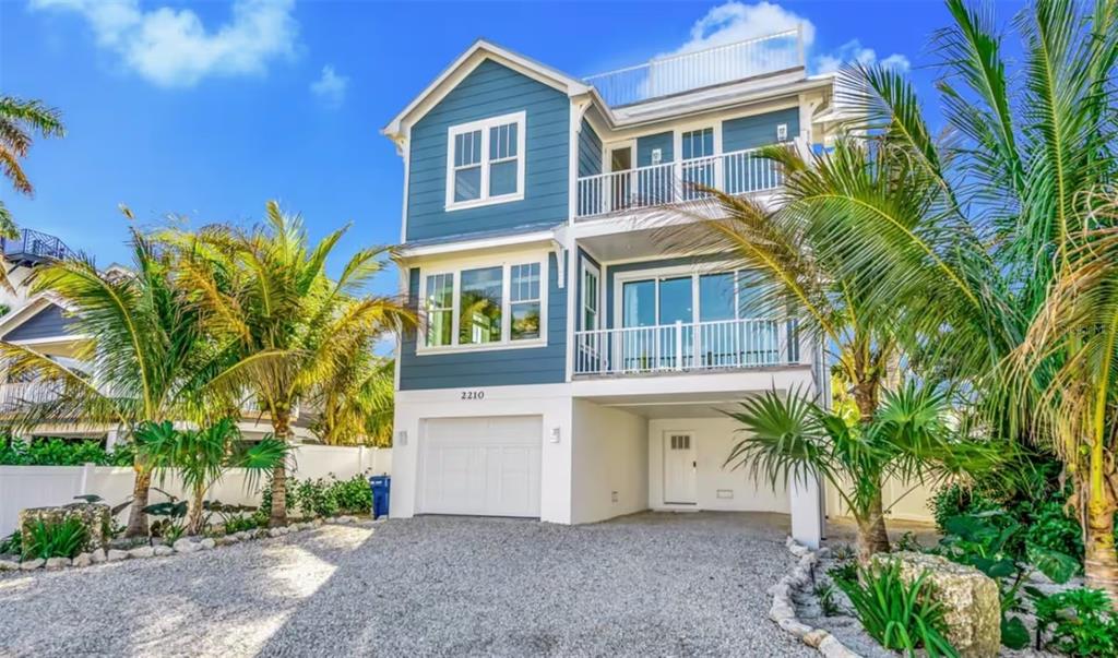 A three-story blue coastal house with a gravel driveway, white trim, and two balconies — 2210 AVENUE A, BRADENTON BEACH, FL