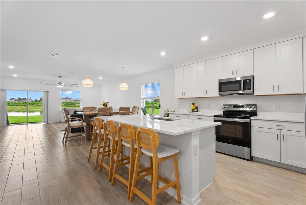 A kitchen with white cabinets, a marble-topped island, and bar stools overlooks a dining area — 10032 LAST LIGHT GLEN, PARRISH, FL