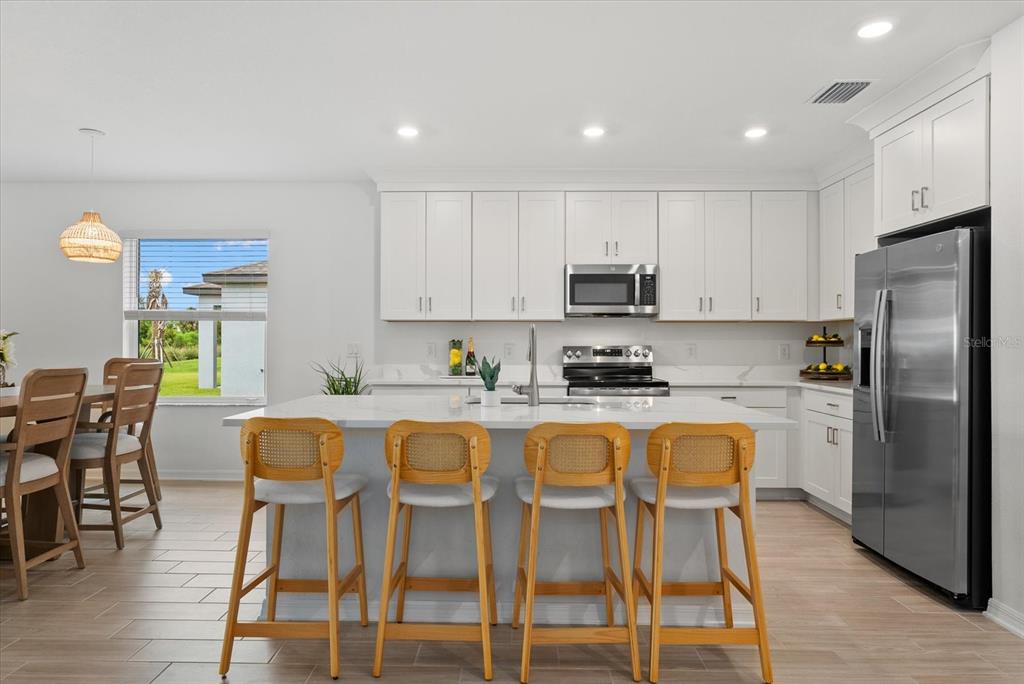 A modern kitchen features white cabinetry, a large center island with four stools, and stainless appliances — 10032 LAST LIGHT GLEN, PARRISH, FL