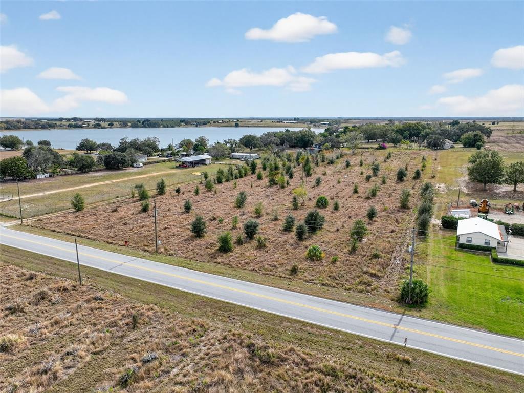 An aerial view shows a vacant, tree-dotted lot adjacent to a road and a lake — FORT MEADE ROAD N, FROSTPROOF, FL