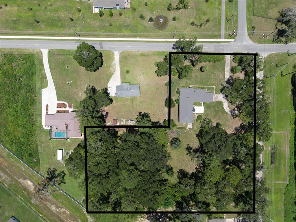This aerial view shows two residential properties with driveways, trees, and a large fenced yard — 2100 NW 21ST STREET, OCALA, FL