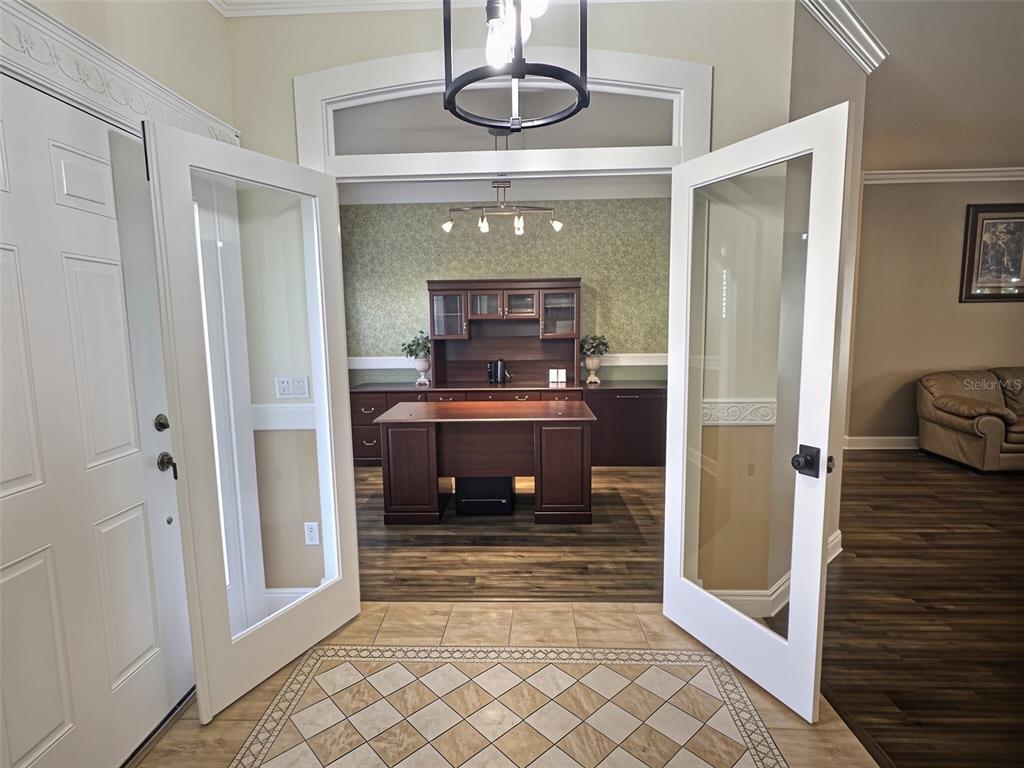 A foyer with tiled flooring leads into a living area with wood-look floors and glass doors — 55 BROOKLYN LANE, PALM COAST, FL