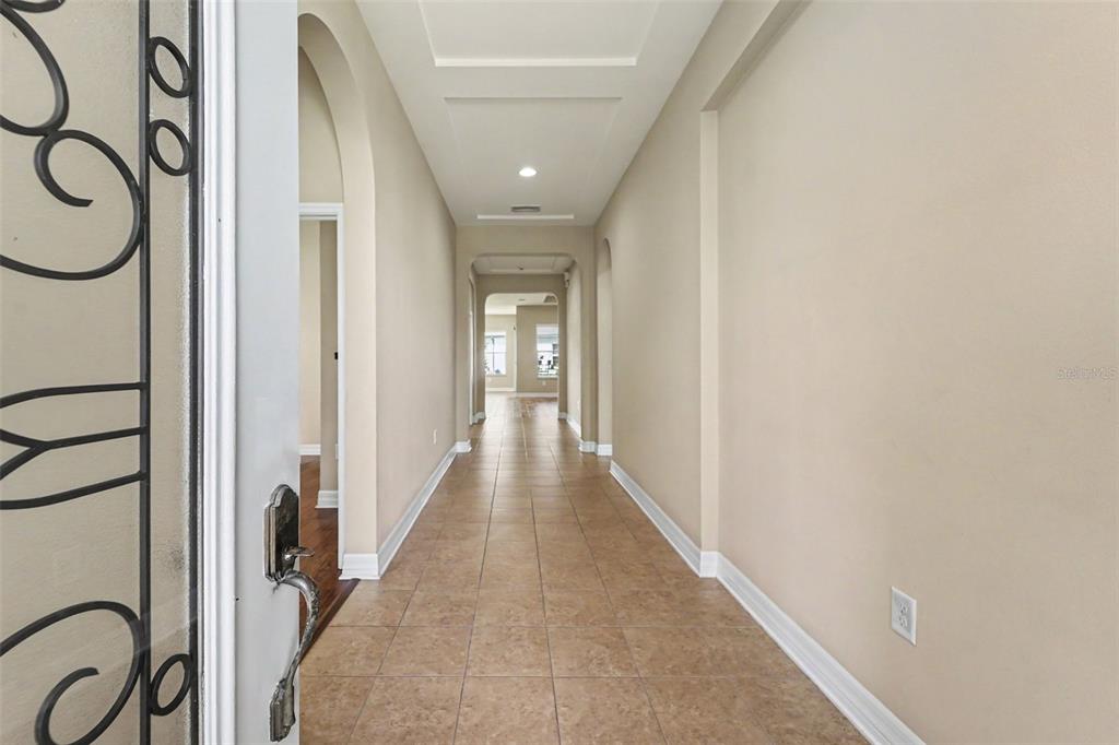 A long, tiled entryway hallway leads to an arched doorway with a view of windows — 2397 GWYNHURST BOULEVARD, WESLEY CHAPEL, FL