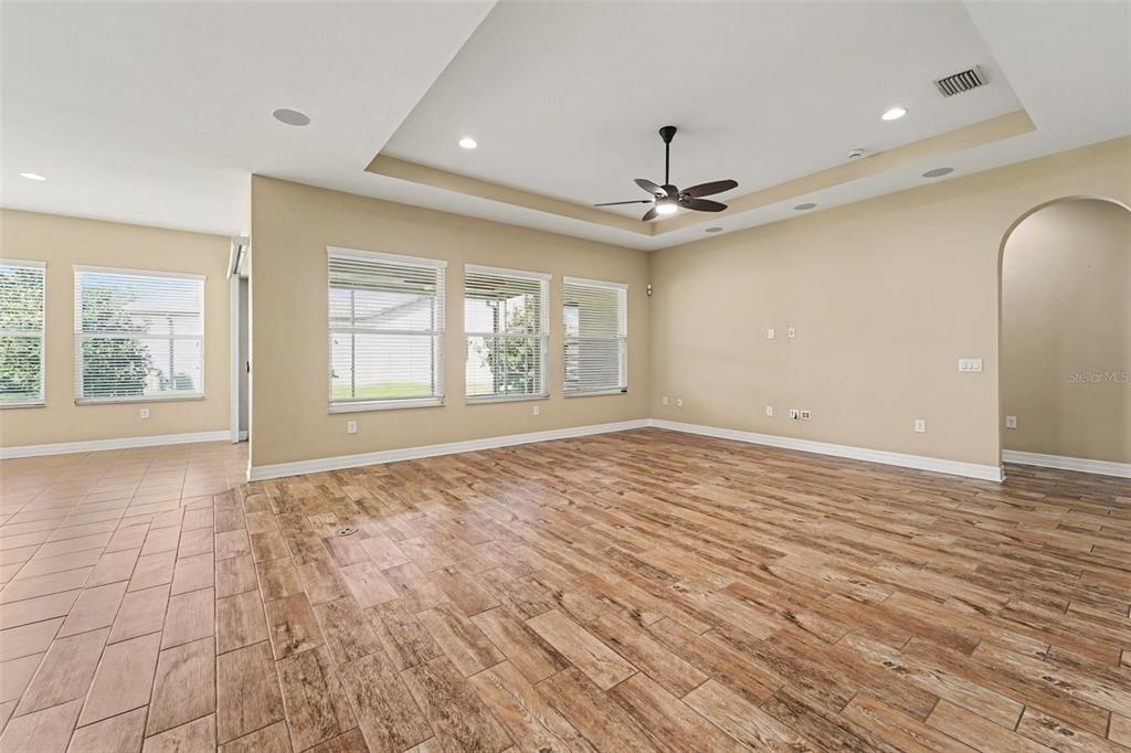 An empty living room features a tray ceiling, a ceiling fan, and wood-look tile flooring — 2397 GWYNHURST BOULEVARD, WESLEY CHAPEL, FL
