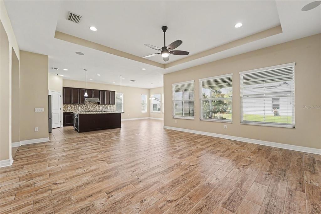 An open-concept living area features wood-look tile flooring, a tray ceiling, and a modern kitchen — 2397 GWYNHURST BOULEVARD, WESLEY CHAPEL, FL