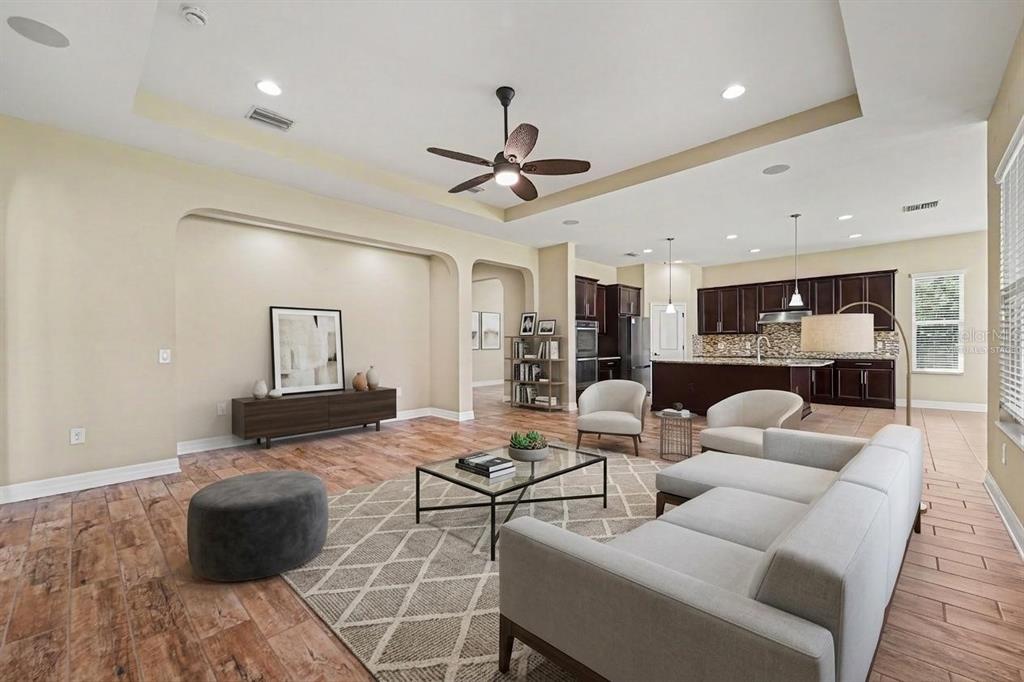 A living room with wood-look tile floors, a tray ceiling, and an open kitchen beyond — 2397 GWYNHURST BOULEVARD, WESLEY CHAPEL, FL
