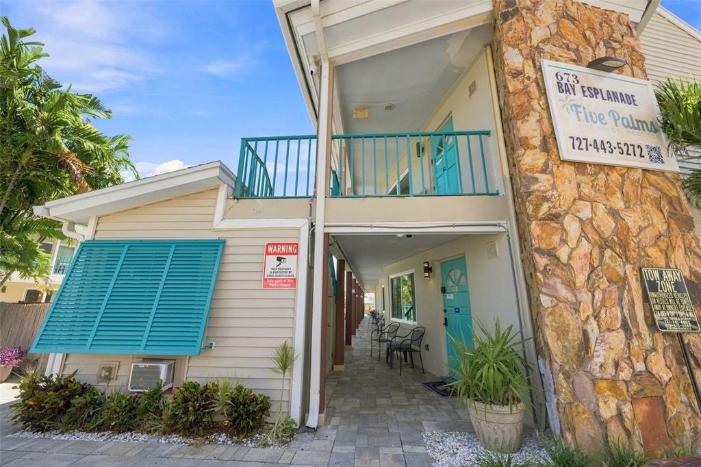 The exterior of a two-story building features teal shutters, a stone facade, and a walkway — 673 BAY ESPLANADE UNIT 109, CLEARWATER, FL