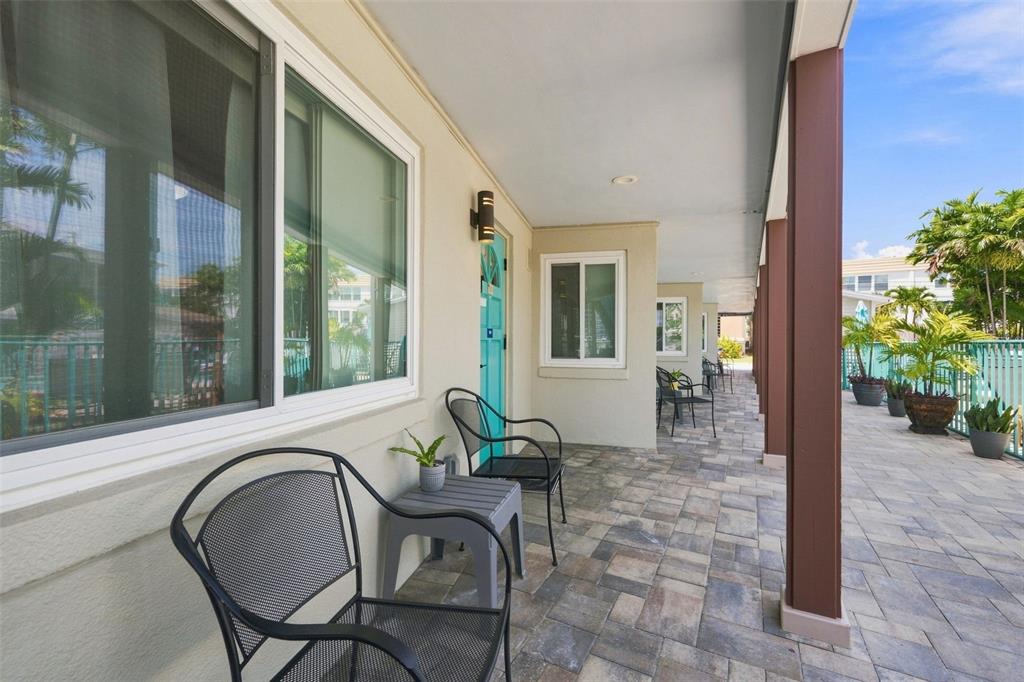 A paved outdoor patio features metal chairs, small tables, and a turquoise door — 673 BAY ESPLANADE UNIT 109, CLEARWATER, FL