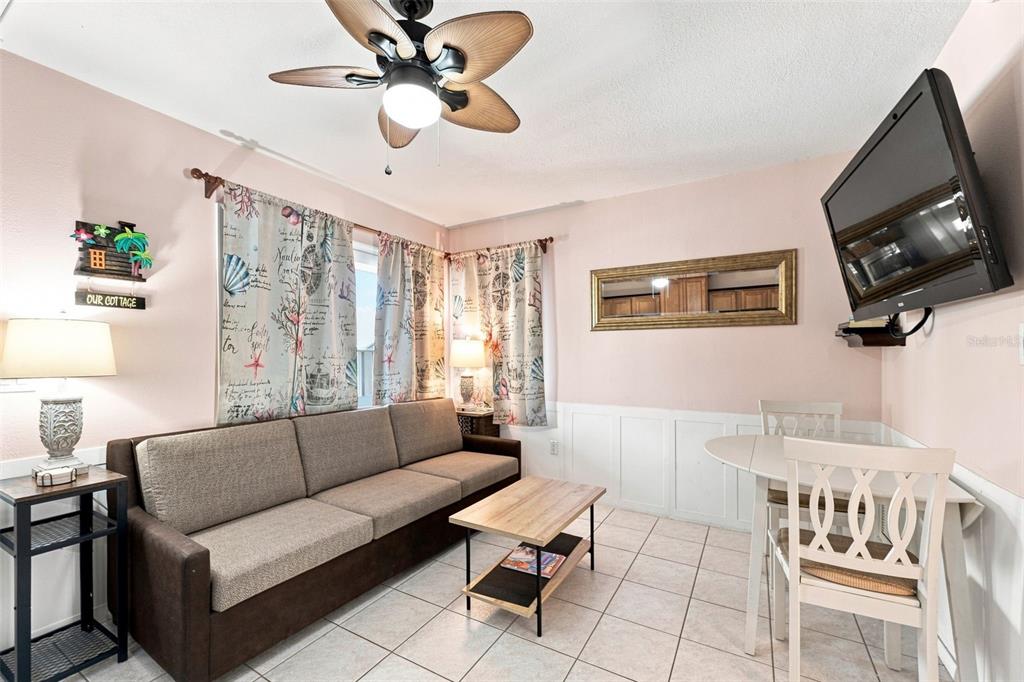 A living room features a brown sofa, a coffee table, a dining set, and tile flooring — 673 BAY ESPLANADE UNIT 109, CLEARWATER, FL