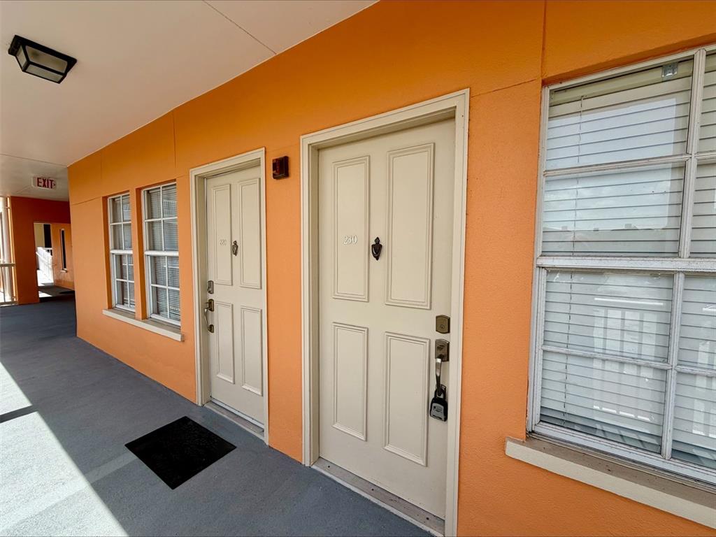 An exterior hallway features orange walls, two beige doors numbered 220 and 230, and windows — 606 MARKET STREET UNIT 230, CELEBRATION, FL