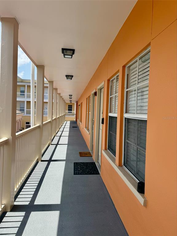An outdoor apartment corridor features orange walls, a gray floor, and a white railing — 606 MARKET STREET UNIT 230, CELEBRATION, FL