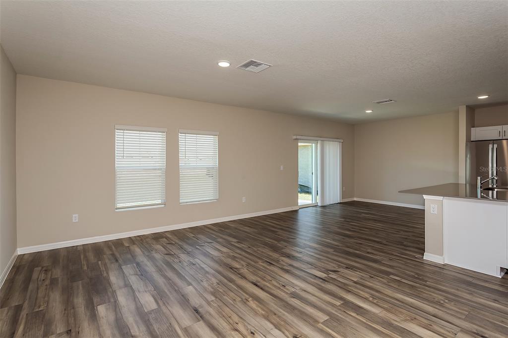 An open-concept living area features wood-look flooring, beige walls, and a sliding glass door — 5394 SAN PIETRO DRIVE, WINTER HAVEN, FL