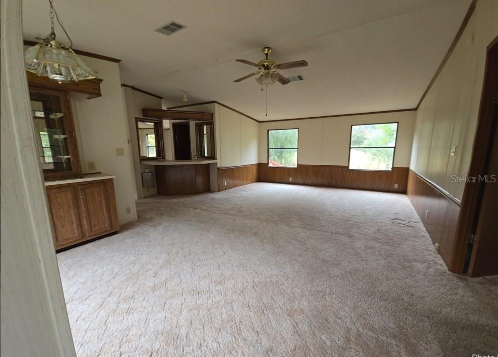 A spacious living room features beige carpeting, wood wainscoting, a ceiling fan, and built-in cabinetry — 12906 NW 38TH AVENUE, REDDICK, FL
