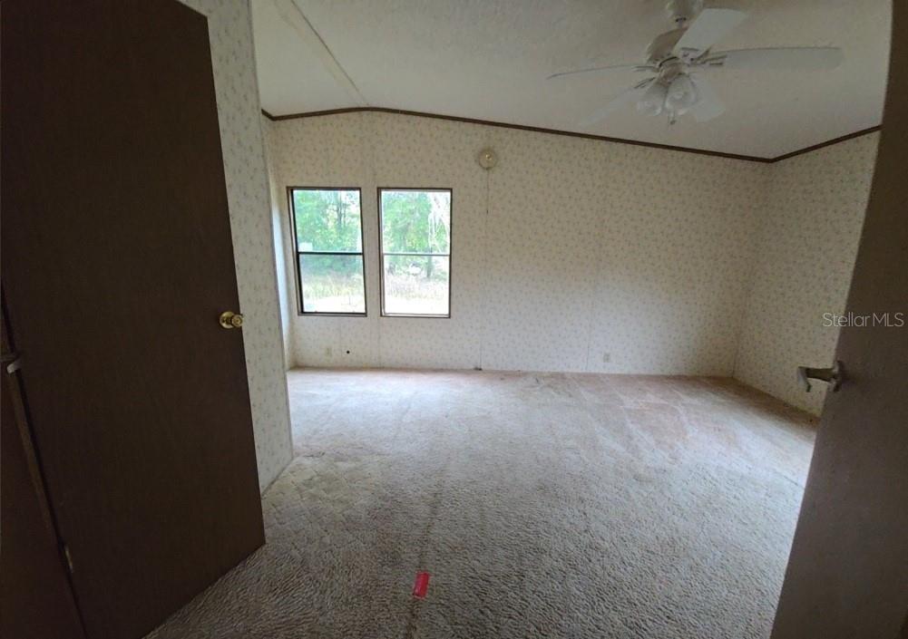 A bedroom with beige patterned wallpaper, tan carpeting, a ceiling fan, and two windows — 12906 NW 38TH AVENUE, REDDICK, FL