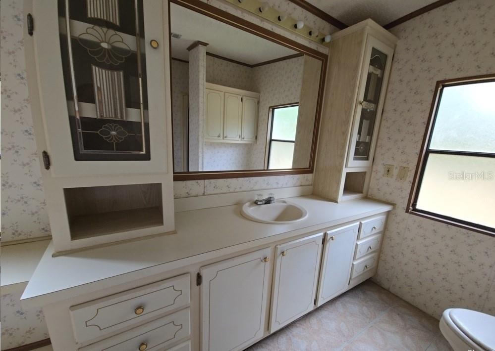 A bathroom features a long vanity with a single sink, wood-trimmed cabinetry, and floral wallpaper — 12906 NW 38TH AVENUE, REDDICK, FL