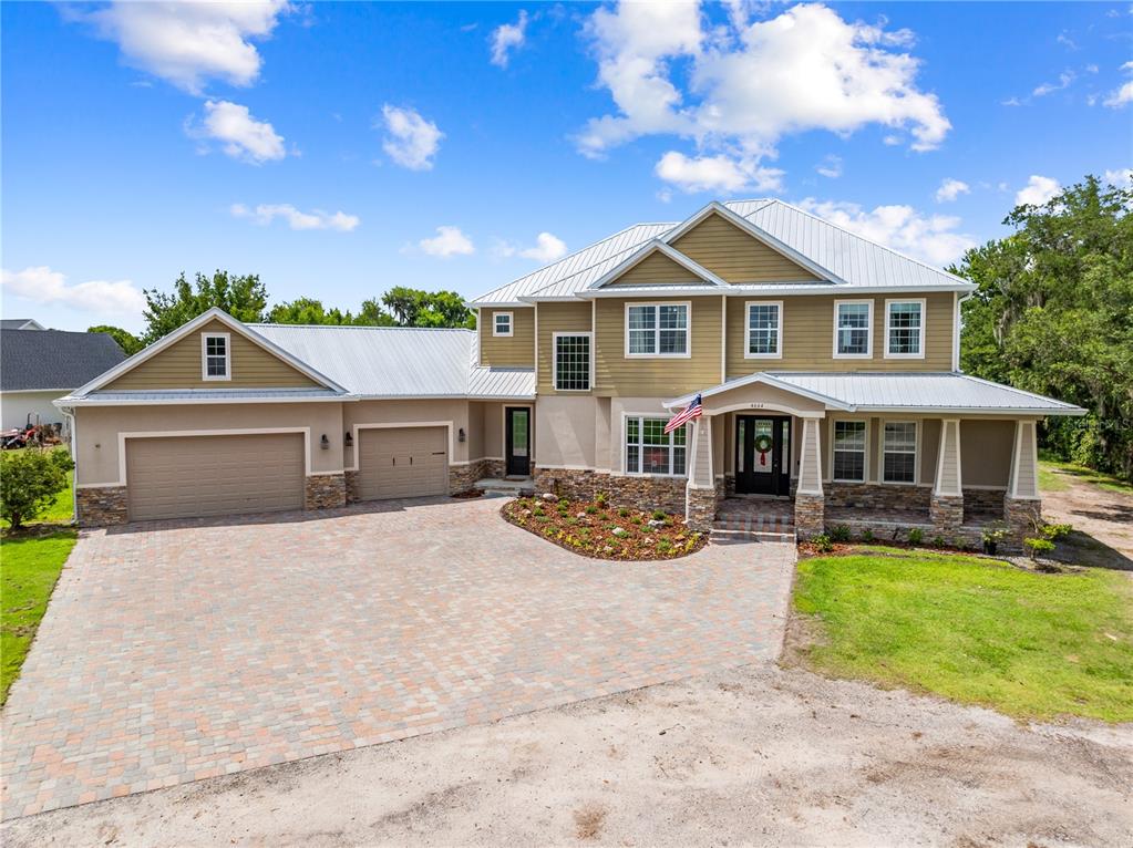 A two-story house with a metal roof, stone accents, and a paved driveway — 4664 HICKORY TREE LN, ST CLOUD, FL