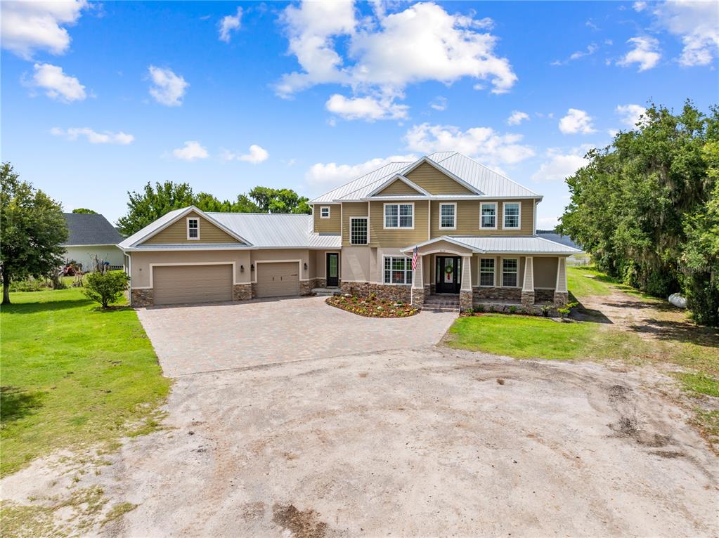 A two-story house with a metal roof, stone accents, and a paved driveway — 4664 HICKORY TREE LN, ST CLOUD, FL