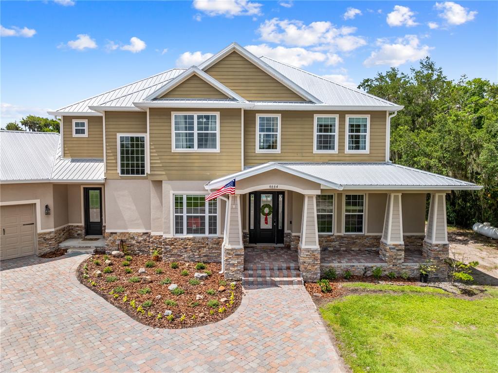 A two-story house features tan siding, a stone base, a metal roof, and a front porch — 4664 HICKORY TREE LN, ST CLOUD, FL