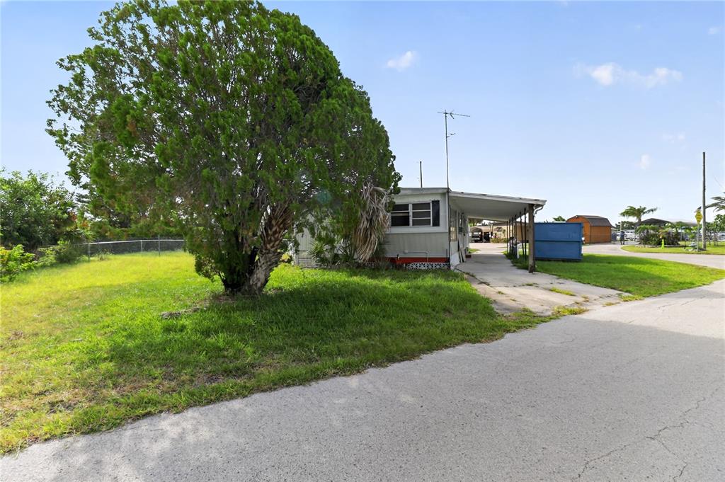 A single-story mobile home with a carport and a large tree in the front yard — 6639 TOWER DRIVE, HUDSON, FL