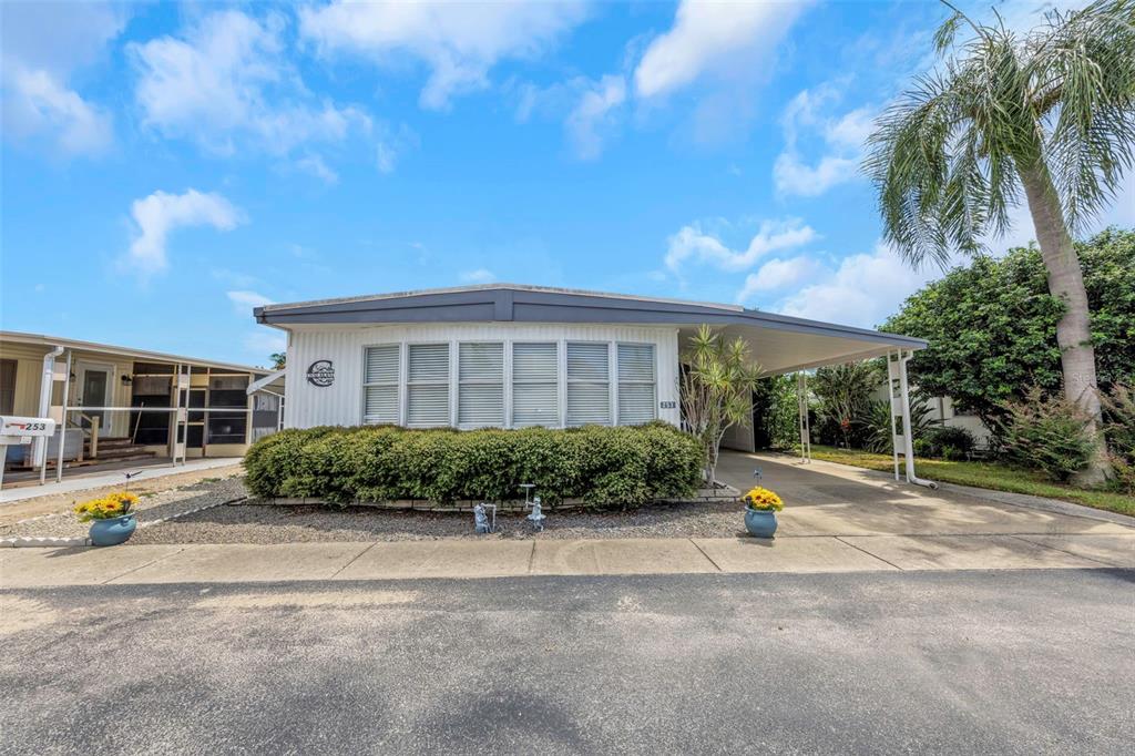 A single-story manufactured home features a carport, a large hedge, and a paved driveway — 3301 US ALT 19 N UNIT 253, DUNEDIN, FL