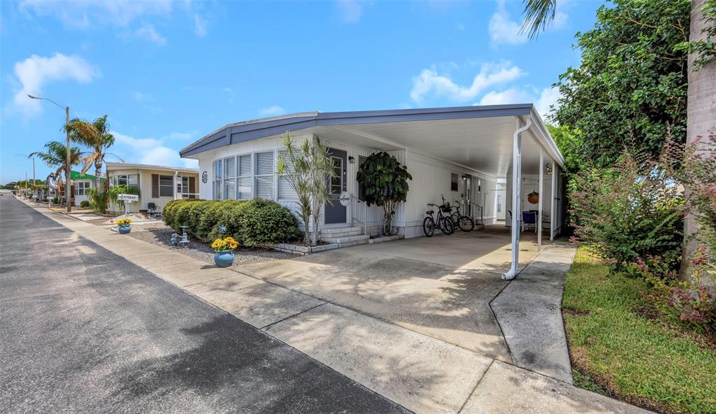 A single-story mobile home features a white exterior, a covered carport, and a landscaped front yard — 3301 US ALT 19 N UNIT 253, DUNEDIN, FL