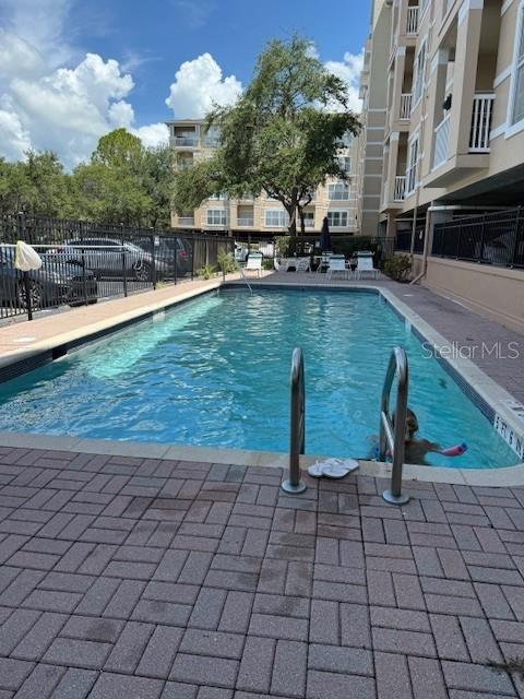 An outdoor swimming pool is surrounded by a brick deck and a multi-story apartment building — 1216 S MISSOURI AVENUE UNIT 214, CLEARWATER, FL