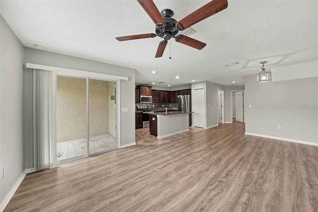 A living room with wood-look flooring leads to a kitchen with dark cabinetry and island — 5042 CHIPOTLE LANE, WESLEY CHAPEL, FL