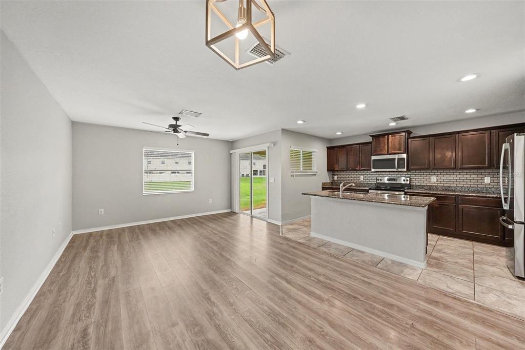 An open-concept kitchen and living area featuring wood-look flooring, dark cabinetry, and a sliding door — 5042 CHIPOTLE LANE, WESLEY CHAPEL, FL
