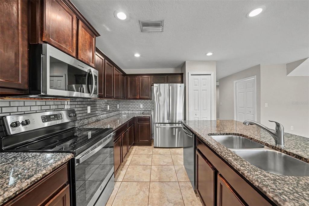 A kitchen features dark wood cabinets, granite countertops, stainless steel appliances, and tile flooring — 5042 CHIPOTLE LANE, WESLEY CHAPEL, FL