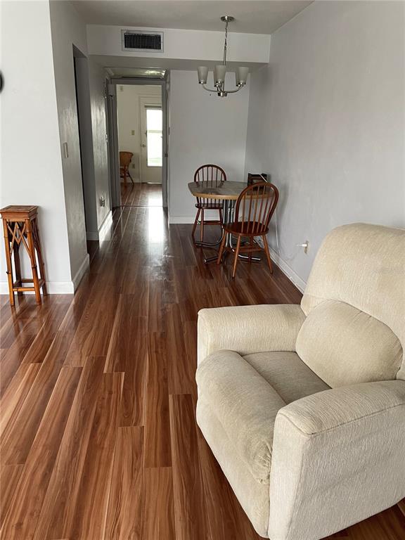A living area with wood-look flooring, a beige recliner, and a dining set near a hallway — 8075 112TH STREET UNIT 203, SEMINOLE, FL