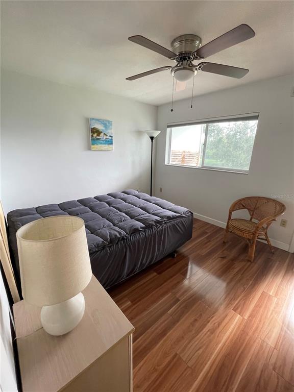A bedroom features a bed with a gray comforter, wood-look flooring, and a ceiling fan — 8075 112TH STREET UNIT 203, SEMINOLE, FL