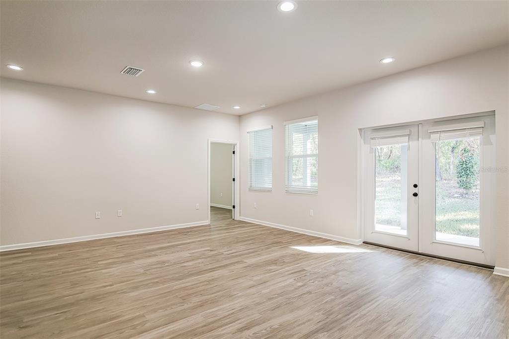 A spacious room with light wood-look flooring, recessed lighting, two windows, and glass double doors — 4744 S RAINBOW DRIVE, INVERNESS, FL
