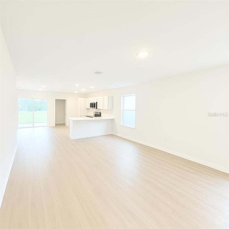 An open-concept kitchen and living area feature light wood-look flooring and white cabinetry — 13013 RED DEER PLACE, PARRISH, FL
