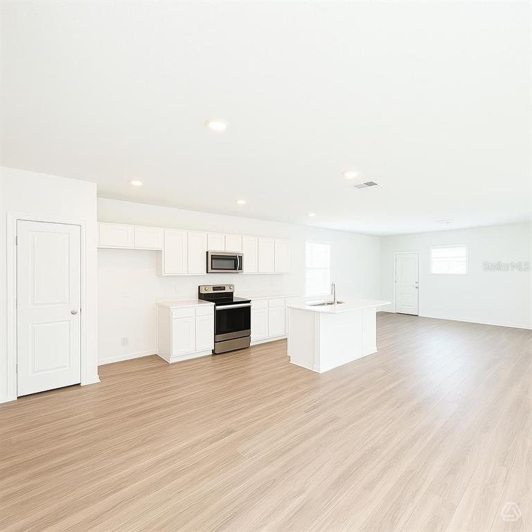 A kitchen with white cabinets, stainless steel appliances, and an island on wood-look flooring — 13013 RED DEER PLACE, PARRISH, FL