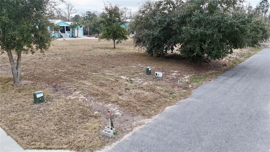 An aerial view shows a vacant, grassy residential lot with utility boxes and a sign — TBD SW 879TH STREET, STEINHATCHEE, FL