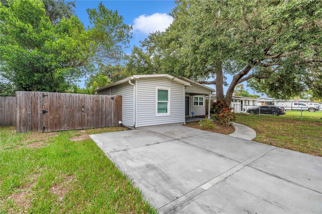 A light-colored house with a concrete driveway and a wooden fence under a large tree — 4411 W LEILA AVENUE, TAMPA, FL