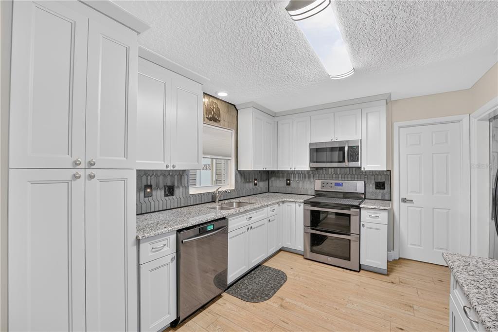 A kitchen with white cabinets, granite countertops, stainless steel appliances, and light wood-look flooring — 28050 LOIS DRIVE, TAVARES, FL