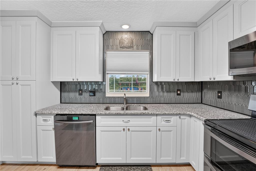 A kitchen features white cabinets, granite countertops, a stainless steel dishwasher, and a gray backsplash — 28050 LOIS DRIVE, TAVARES, FL