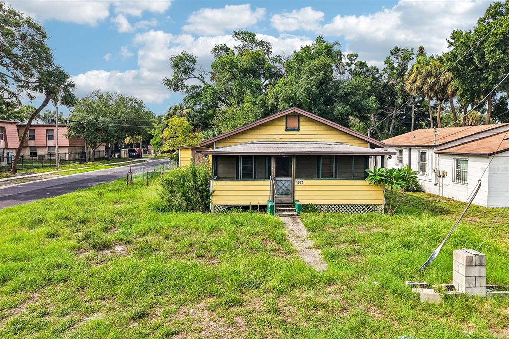 A yellow single-story house with a screened front porch sits on a grassy lot — 1002 W NASSAU STREET, TAMPA, FL