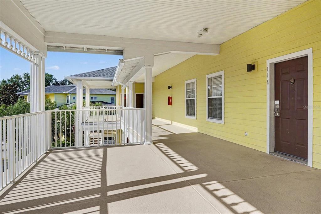 A covered outdoor walkway with a concrete floor, white railings, and a yellow exterior wall — 114 LUCAYA LOOP UNIT 114, DAVENPORT, FL