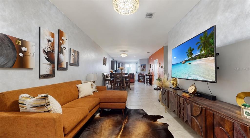 A living room features an orange sectional sofa, a cowhide rug, and a wall-mounted television — 1452 SE 24TH AVENUE, HOMESTEAD, FL