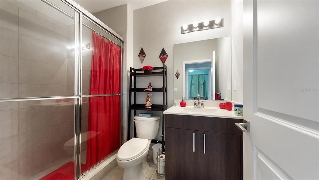 A bathroom features a glass-enclosed shower, a toilet with shelving, and a dark wood vanity — 1452 SE 24TH AVENUE, HOMESTEAD, FL