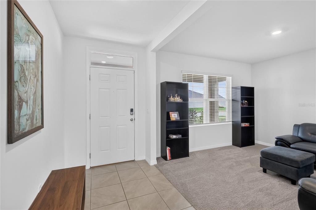 A living room with tile flooring near the entrance, carpeted seating area, and two black bookshelves — 787 AUBURN GROVE CT., AUBURNDALE, FL